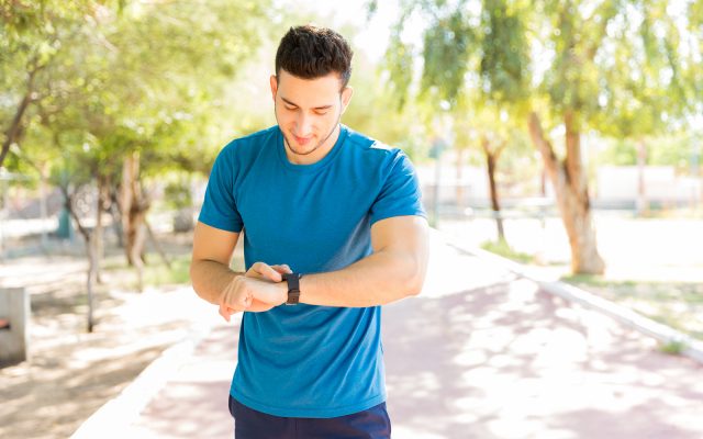Athletic young man checking step counts on smart watch in park during sunny day